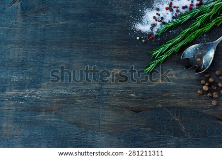 Top view of herbs and spices (rosemary, salt and pepper) on dark wooden background.
