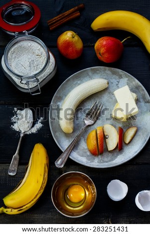 Baking ingredients for cake (flour in glass jar, eggs, butter and fruits)  over rustic wooden board from above. Cooking concept.