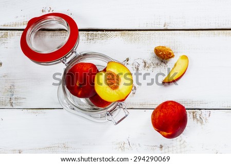 Juicy peaches in glass jar over white wooden background. Top view.