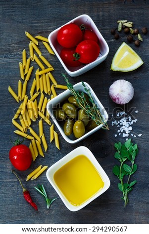 Ingredients for italian pasta with olives, herbs, spices, tomatoes and olive oil on dark wooden background. Vegetarian food, health or cooking concept.
