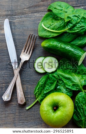 Dining fork and knife with fresh green vegetables on dark wooden background. Detox, diet or healthy food concept.