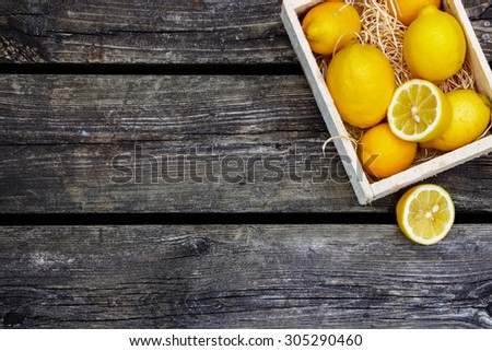 Juicy whole lemons and freshly cut half on rustic wooden background with space for text. Top view.