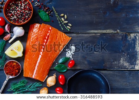 Salmon fish on dark wooden background with space for text. Fish with aromatic herbs, spices and vegetables - healthy food, diet or cooking concept