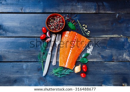 Food background with fresh salmon fish on dark wooden board. Fish with aromatic herbs, spices and vegetables - healthy food, diet or cooking concept.