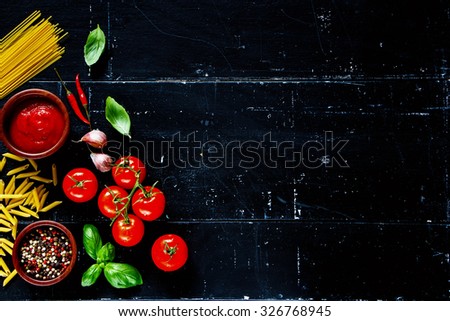 Italian pasta with basil leaves, spices, herbs and tomato sauce on dark vintage background with space for text. Vegetarian food, diet, health or cooking concept.