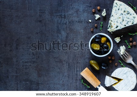 Cheese variety, olives and fresh herbs over dark vintage texture. Top view. Background layout with free text space.