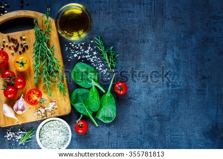 Organic vegetarian ingredients, olive oil and seasoning on rustic wooden cutting board over dark vintage background with space for text, top view. Healthy food, vegan or diet nutrition concept.