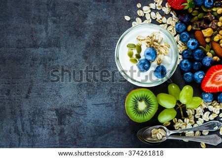 Close up of tasty ingredients (oat flakes, kiwi, berries with yogurt and seeds) for breakfast or smoothie on dark vintage background - Healthy food, Diet, Detox, Clean Eating or Vegetarian concept.