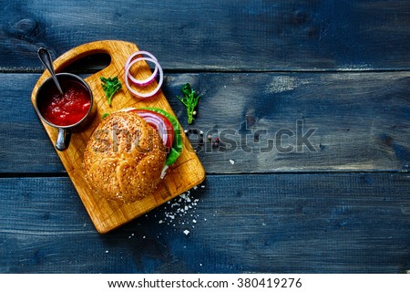 Vegan burger with fresh vegetables on dark  rustic wooden table, top view, border. Healthy fast food background with space for text.