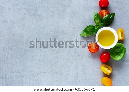 Red and yellow cherry tomatoes, olive oil with fresh basil leaves on light grey table, top view. Simple Italian food concept background with space for text.