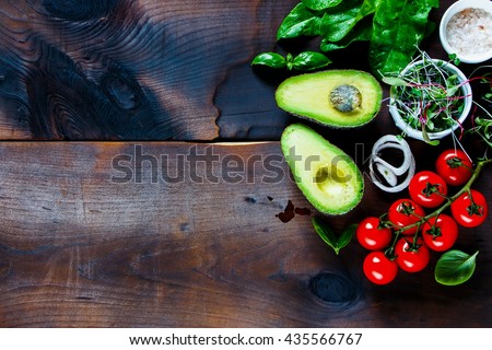Healthy organic ingredients for salad making: avocado, spinach, tomatoes, sprouts, basil, olive oil on rustic background, top view. Flat lay with place for text. Vegan and healthy food concept