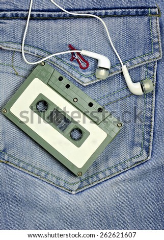 Vintage tape cassette and white earphones on jean background.