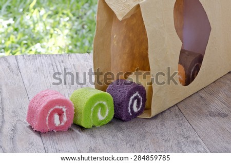 Colorful of cream role cake in paper bag on wooden background.