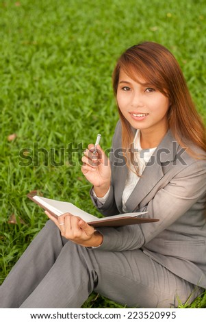Business woman thinking solution on lunch break in city park. Young professional businesswoman sitting and thinking on green grass in city park.