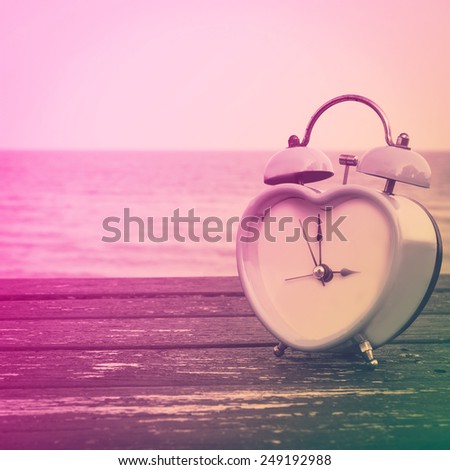 retro clock on wooden floor and blue sea, summer time on the beach vintage color tone.