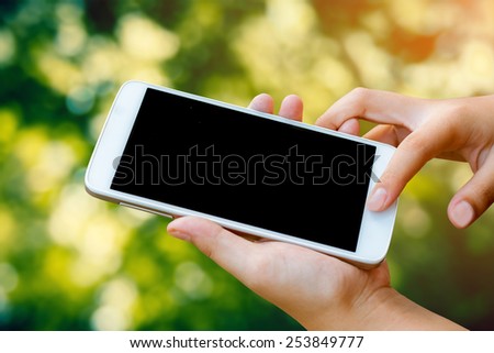 woman hand hold and  touch screen smart phone, tablet,cellphone on day noon light with green blurred nature background.