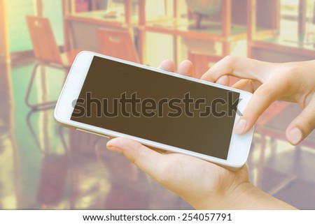young woman hand hold and touch screen smart phone,tablet,cellphone in classroom,vintage color tone.