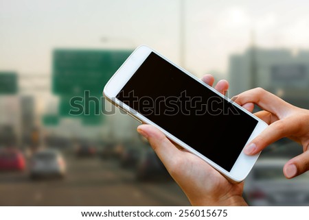 woman hand hold and touch screen smart phone, tablet,cellphone on city traffic in morning background.