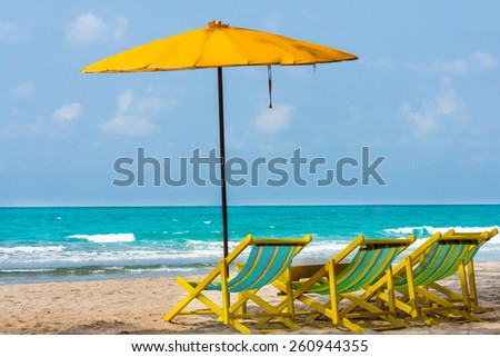 yellow beach chair on sand under shadow of beach umbrella  with blue sea background.