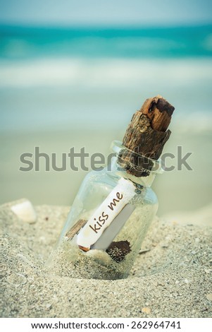 bottle with a message kiss me on white sand beach over blue sea and sun light.