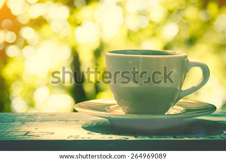 white cup of coffee or tea  on wooden table in garden with sun lighting.