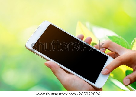 woman hand hold and touch screen smart phone, tablet,cellphone on day noon light with green blurred nature background.