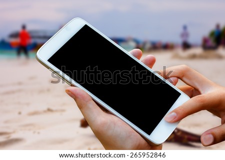 woman hand hold and touch screen smart phone, tablet,cellphone on blurred beautiful beach background.