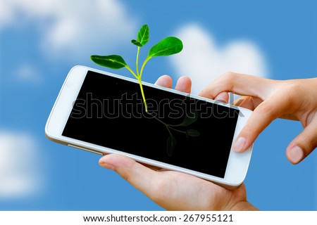 woman hand holding and touch screen of smart phone,tablet,cellphone with seedling growing up on screen over blue and cloudy sky. abstract background to green communication technology concept.