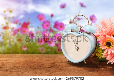 old retro clock on wooden floor over cosmos field and sunlight on day noon background.