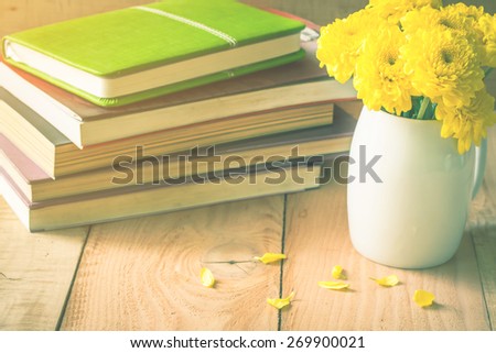selective focus of yellow flower in white pot on wooden floor with old book, vintage color tone.