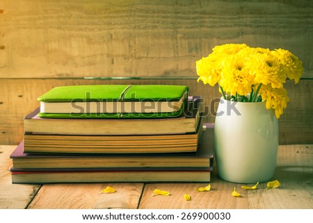 selective focus of yellow flower in white pot on wooden floor with old book, vintage color tone.