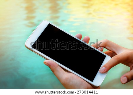 woman hand hold and touch screen smart phone, tablet,cellphone on blurred water background.