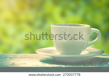 white cup of coffee or tea on wooden table in garden with sun lighting.