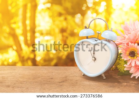 old retro clock on wooden floor over bokeh of garden and sunlight on day noon background.