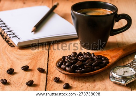 selective focus of coffee beans on wooden spoon with notebook and cup of espresso ,vintage color tone.