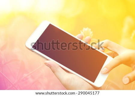 woman hand hold and touch screen smart phone, tablet,cellphone on day noon light with autumn blurred nature background, vintage color tone.