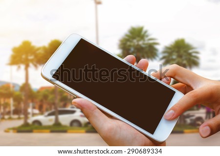 woman hand hold and touch screen smart phone, tablet,cellphone over blurred car parking background in morning.