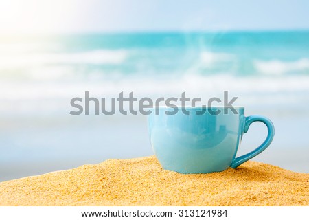 blue cup of coffee on white sand beach over blue sky and sea on day noon light background.