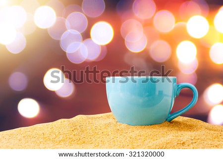 blue cup of coffee or tea on sand over bokeh background.