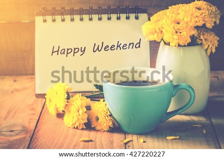 blue cup of coffee on wooden floor with yellow flower in white pot and happy weekend note on morning sunlight. vintage color tone, happy weekend concept.