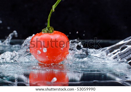 Red tomato with green stalk and splash water over black background