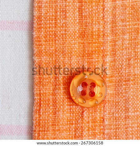 Planck orange shirt with a button on a white cotton fabric closeup