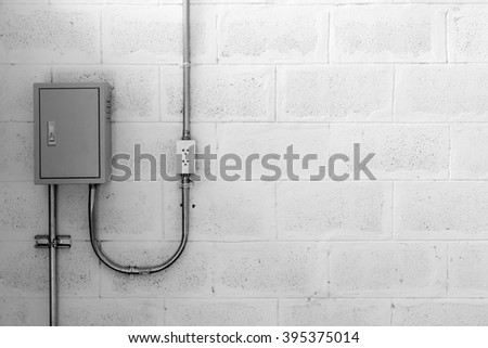 electric box on concrete wall with steel tube and plug, black and white