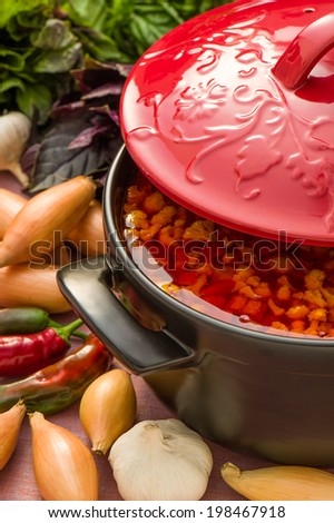 Cold vegetable soup in a black ceramic pot with red cover