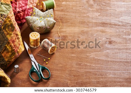Spools of threads, needle, thimble, scissors and pin cushion on a wood background