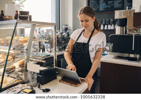 Portrait of young caucasian female woman cashier. Seller using touch pad for accepting client customer payment. Small business of coffee shop cafeteria.