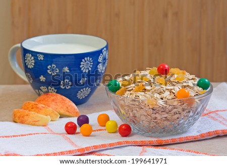 Bowl of oatmeal with raisins and colorful small round candies, blue cup of milk, slices of apple on a wooden background. Selective focus.