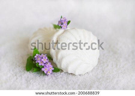 White marshmallows and lilac forget-me-not flowers with green leaves on a white background. Selective focus