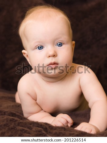 Closeup portrait of a cute blond baby girl with blue eyes with curious expression on her face.