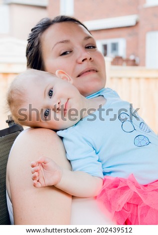 Portrait of mother with daughter relaxing on her shoulder smiling outdoor backyard summer